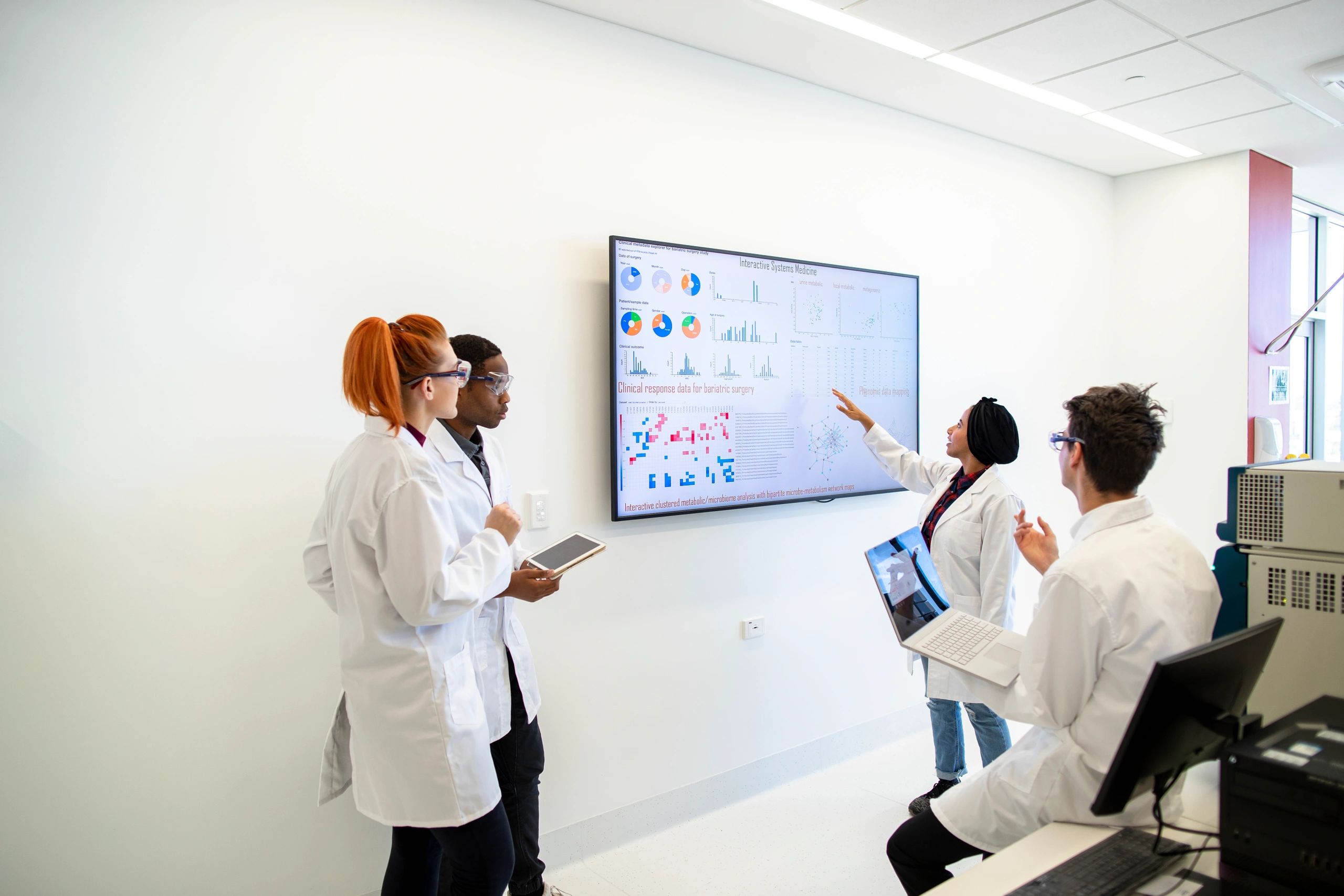 Multidisciplinary medical research team of engineers, computer scientists, biologists, and clinicians collaborating around a digital display